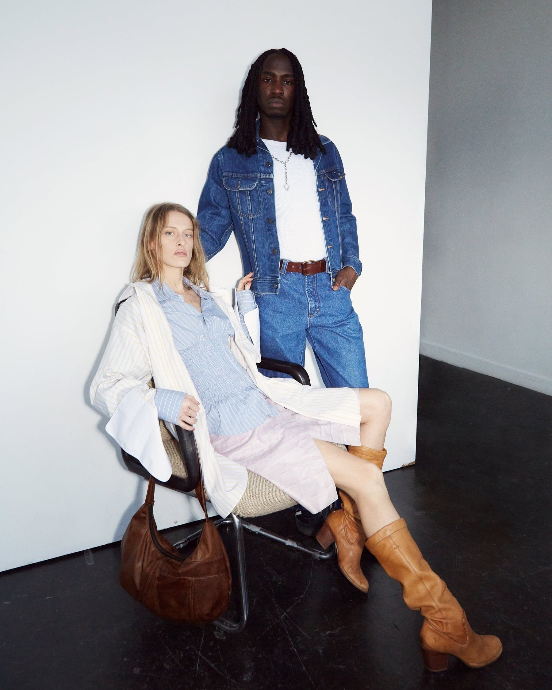 Zolaqlı köynək və açıq qəhvəyi çəkmədə oturan model, yanında denim gödəkçə və cins şalvarda ayaq üstə model